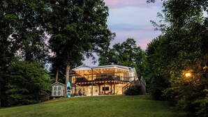 A modern house with a large glass front, a covered porch, and a small adjacent building. - Lakefront + Kayaks + Dock + Screened in Porch | Home Sweet Bowen (Inman)