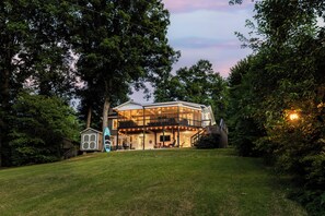 A modern house with a large glass front, a covered porch, and a small adjacent building.