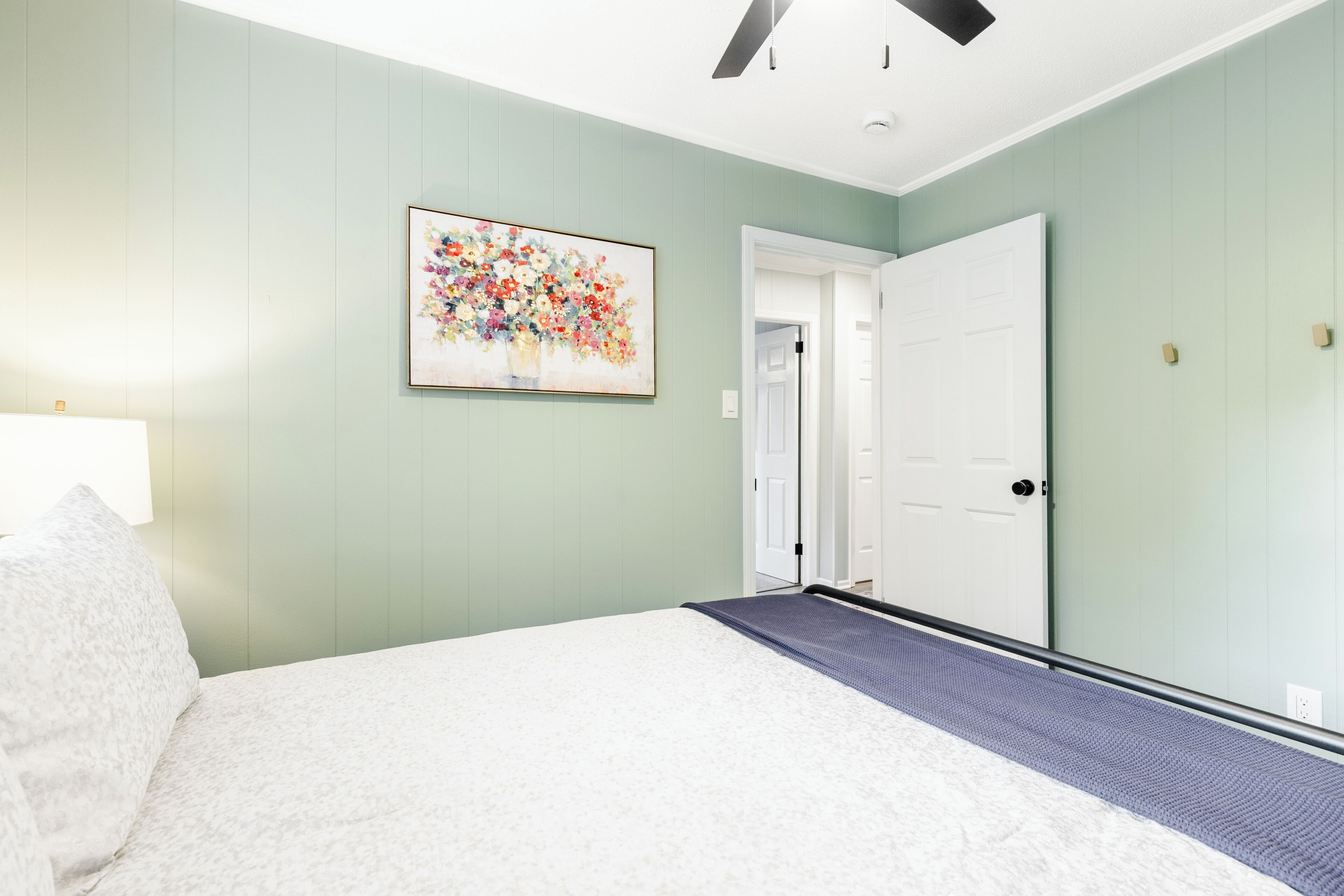 A bedroom with a bed, a door, and a wall-mounted painting.
