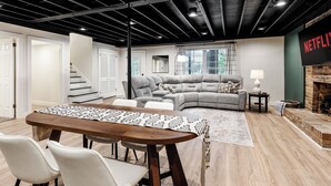 A modern living room with a dining area, a fireplace, and a Netflix sign. - Lakefront + Kayaks + Dock + Screened in Porch | Home Sweet Bowen (Inman)