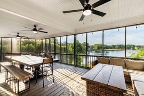 A spacious deck with a dining table, chairs, and a sofa, overlooking a lake.