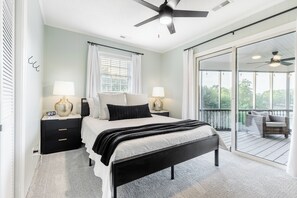 Ein Schlafzimmer mit Bett, Nachttischen, Lampen, einem Deckenventilator und einem Balkon mit Stuhl.
