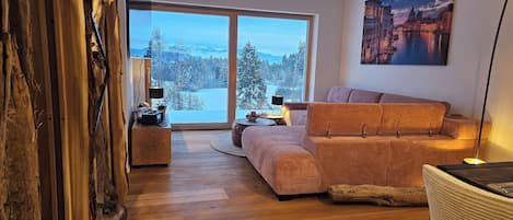 A modern living room with a large window, a sofa, a coffee table, and a painting on the wall.