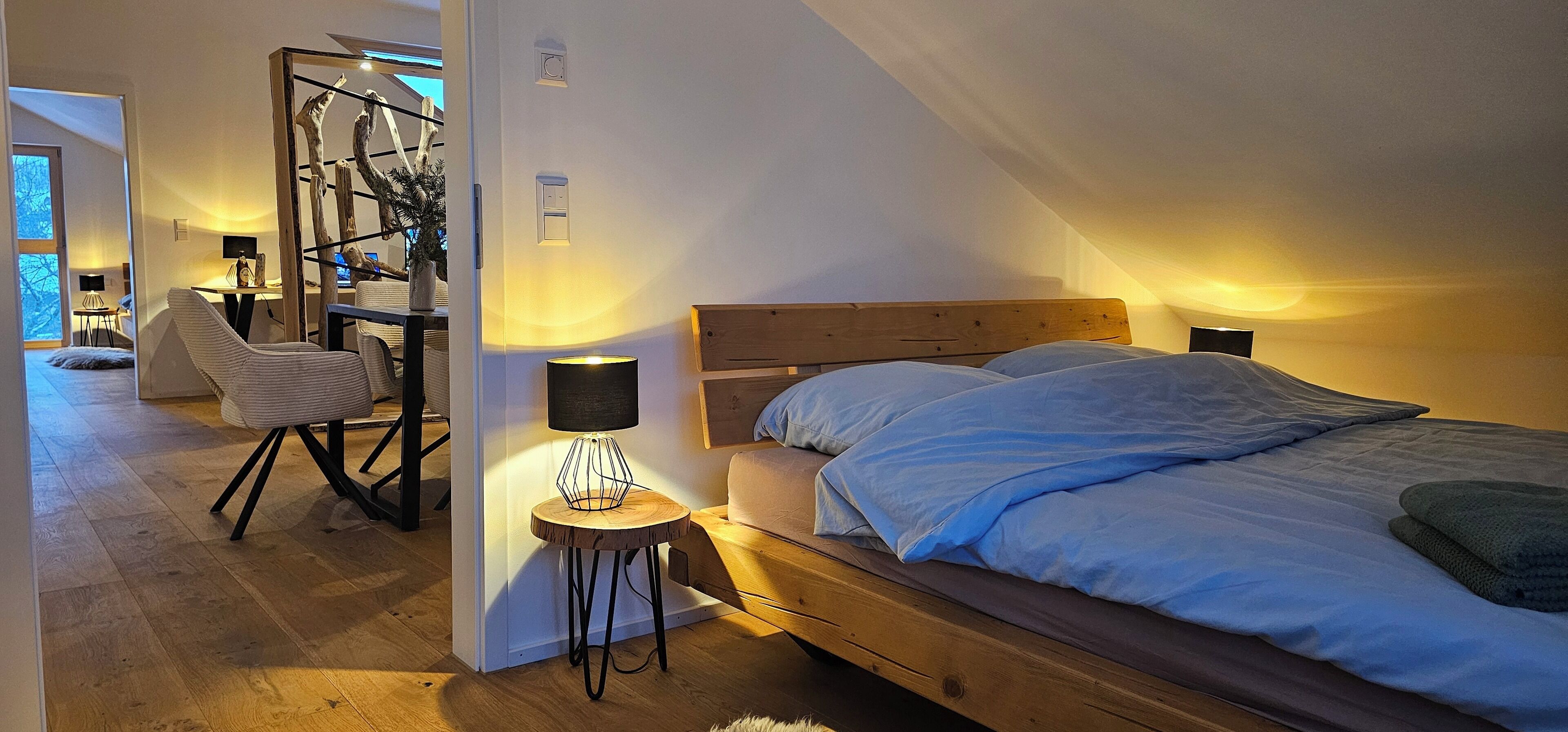 Un dormitorio con cabecera de madera, cama con ropa de cama azul, mesita de noche con lámpara y escritorio con silla.