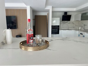 A modern kitchen with a marble countertop, a bottle of Tom Tom Saint James, and a tray with glass jars.