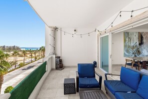 Ein Balkon mit Blick auf den Strand, einem Tisch mit Stühlen und einem Bild an der Wand.