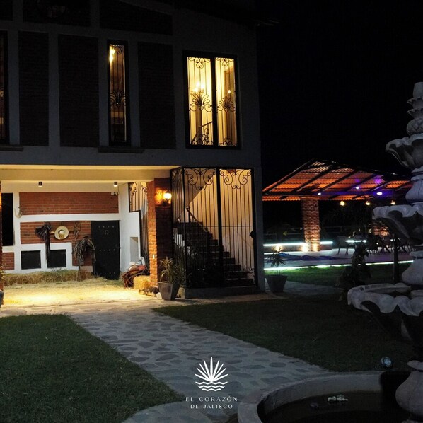 Un edificio de dos pisos con una entrada bien iluminada, una escalera y un área exterior cubierta con una fuente decorativa.