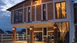 Ein zweistöckiges Haus mit überdachter Terrasse, großen Fenstern und einer Treppe, die zu einer oberen Ebene führt.