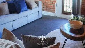 Ein Zimmer mit einem hellblauen Sofa an einer Ziegelwand, einem runden Holztisch mit einer Schüssel und einem Fenster mit Vorhängen.