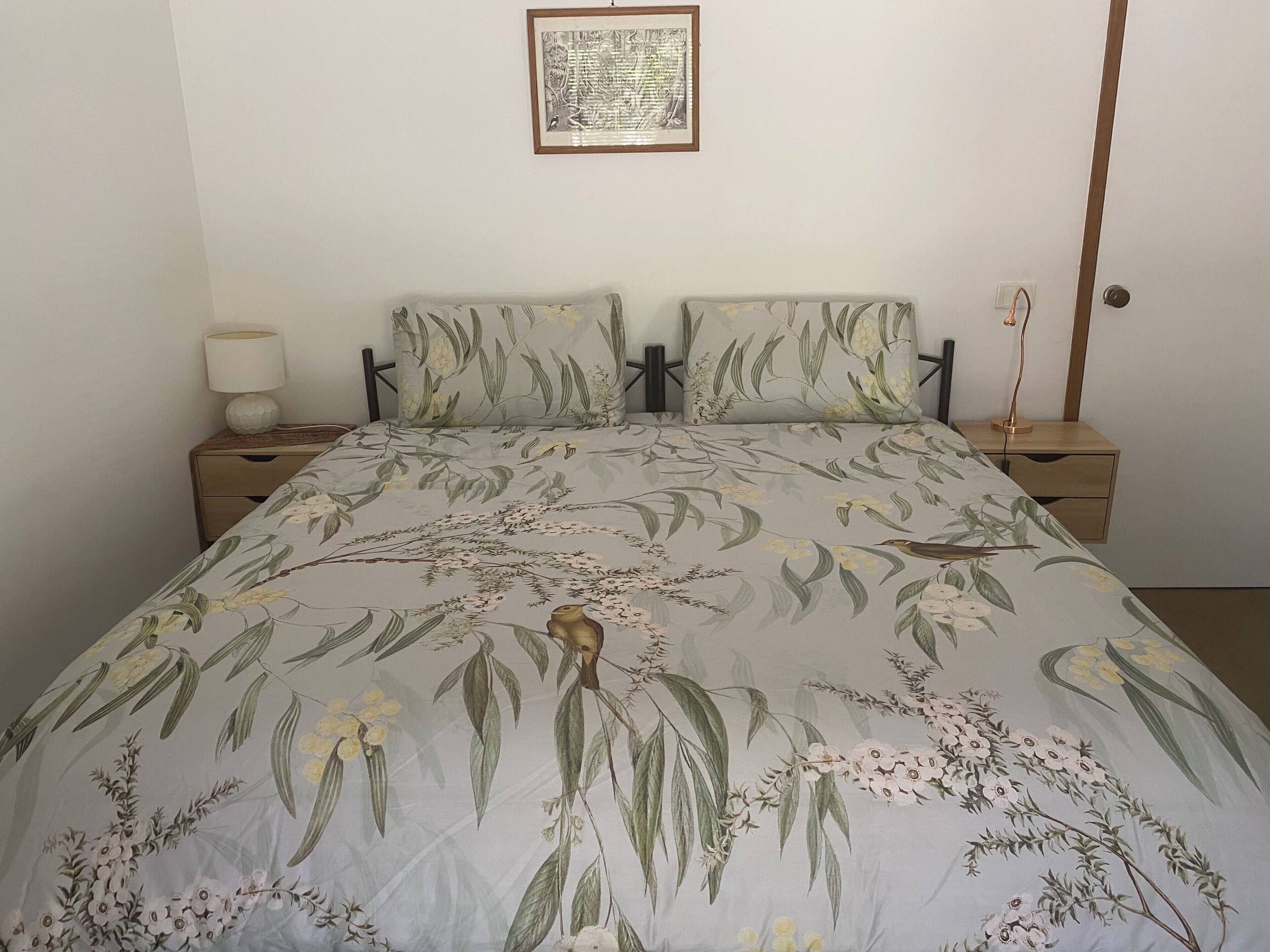 A bedroom with a bed, two nightstands, a lamp, and a framed picture on the wall.