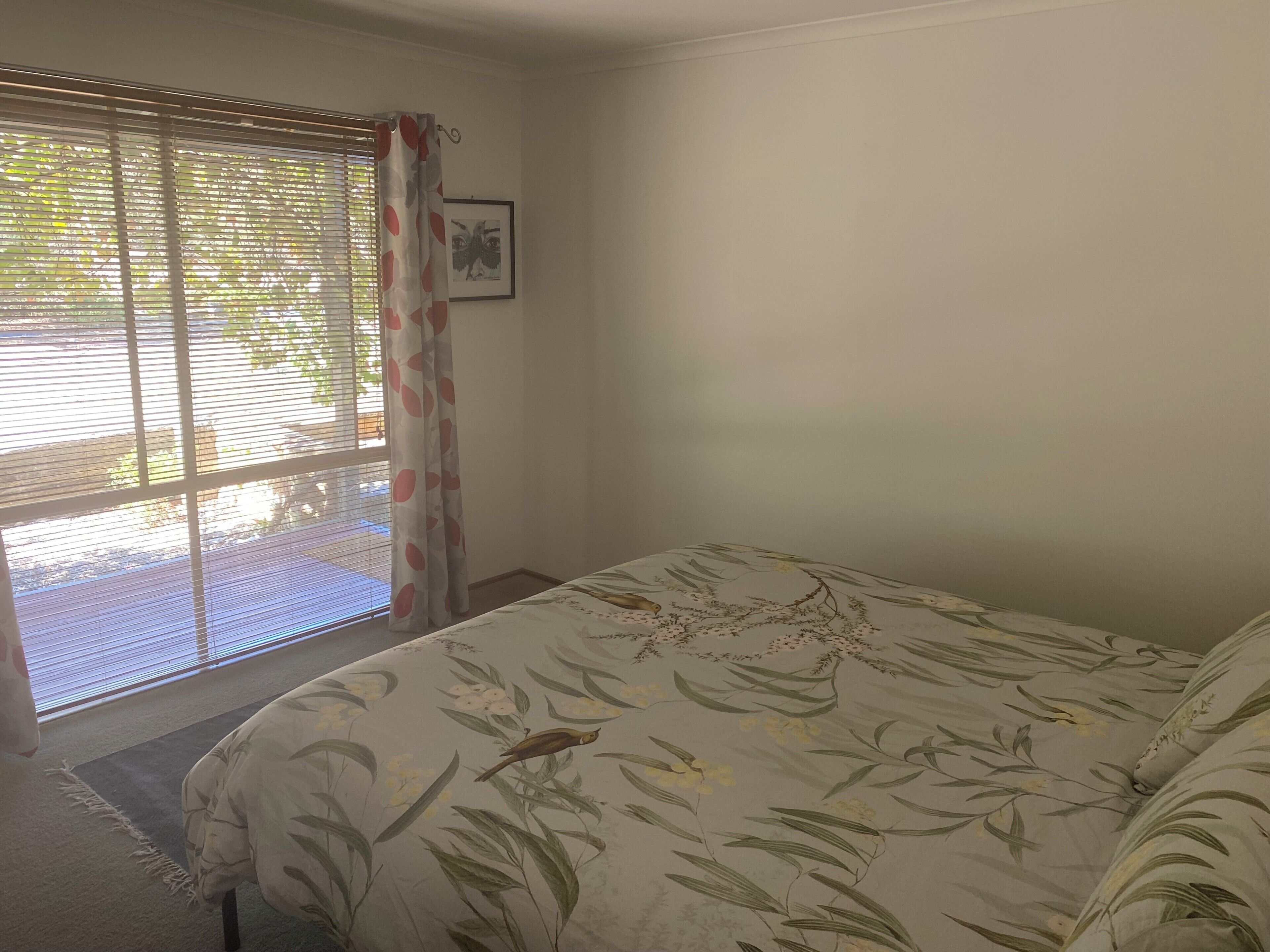A bedroom with a bed, a window with blinds, a curtain, and a picture on the wall.