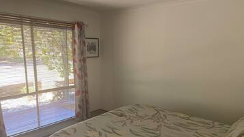 A bedroom with a bed, a window with blinds, a curtain, and a picture on the wall.