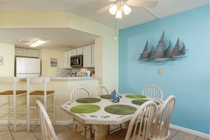 A dining area with a table set for four, surrounded by white chairs with green placemats. A ceiling fan is above the table, and a sailboat decoration hangs on the blue wall. - Panaramic oceanfront views abound lazy river pools kitchen washer dryer (Myrtle Beach)