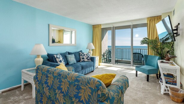 Een kamer met een blauwe muur, een bank, een stoel, een kleine tafel en een balkon met uitzicht op zee.