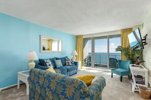 A room with a blue wall, a sofa, a chair, a small table, and a balcony with a view of the sea. - Panaramic oceanfront views abound lazy river pools kitchen washer dryer (Myrtle Beach)
