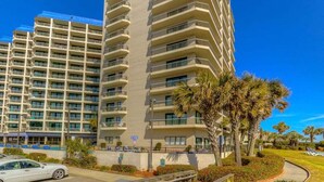 A multi-story hotel with balconies, a parking area, and palm trees. - Oceanfront resort with all amenities (Myrtle Beach)