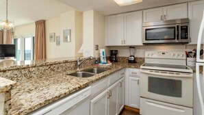 A kitchen with granite countertops, white cabinets, a microwave, an oven, and a coffee maker. - Oceanfront resort with all amenities (Myrtle Beach)