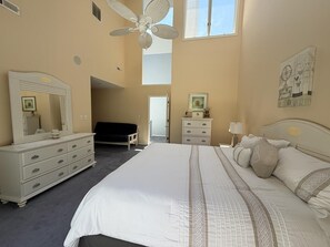 A bedroom with a large bed, a dresser, a chair, a desk, a ceiling fan, and a window. - Pool. Close to Beach. Sleeps 11 Guests (Villas)