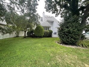A residential house with a well-maintained lawn, a white picket fence, and a large tree in the foreground. - Pool. Close to Beach. Sleeps 11 Guests (Villas)