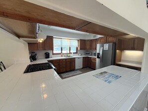 A kitchen with white tiles, wooden cabinets, a gas stove, a refrigerator, and a window with curtains. - Pool. Close to Beach. Sleeps 11 Guests (Villas)