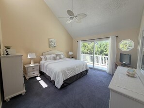 A bedroom with a bed, nightstands, a dresser, a ceiling fan, a television, and a balcony with a view of trees. - Pool. Close to Beach. Sleeps 11 Guests (Villas)