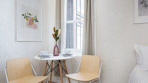 Ein Zimmer mit einem Bett, einem Vorhangfenster, einem Tisch mit Stühlen und einer Blumenvase.
