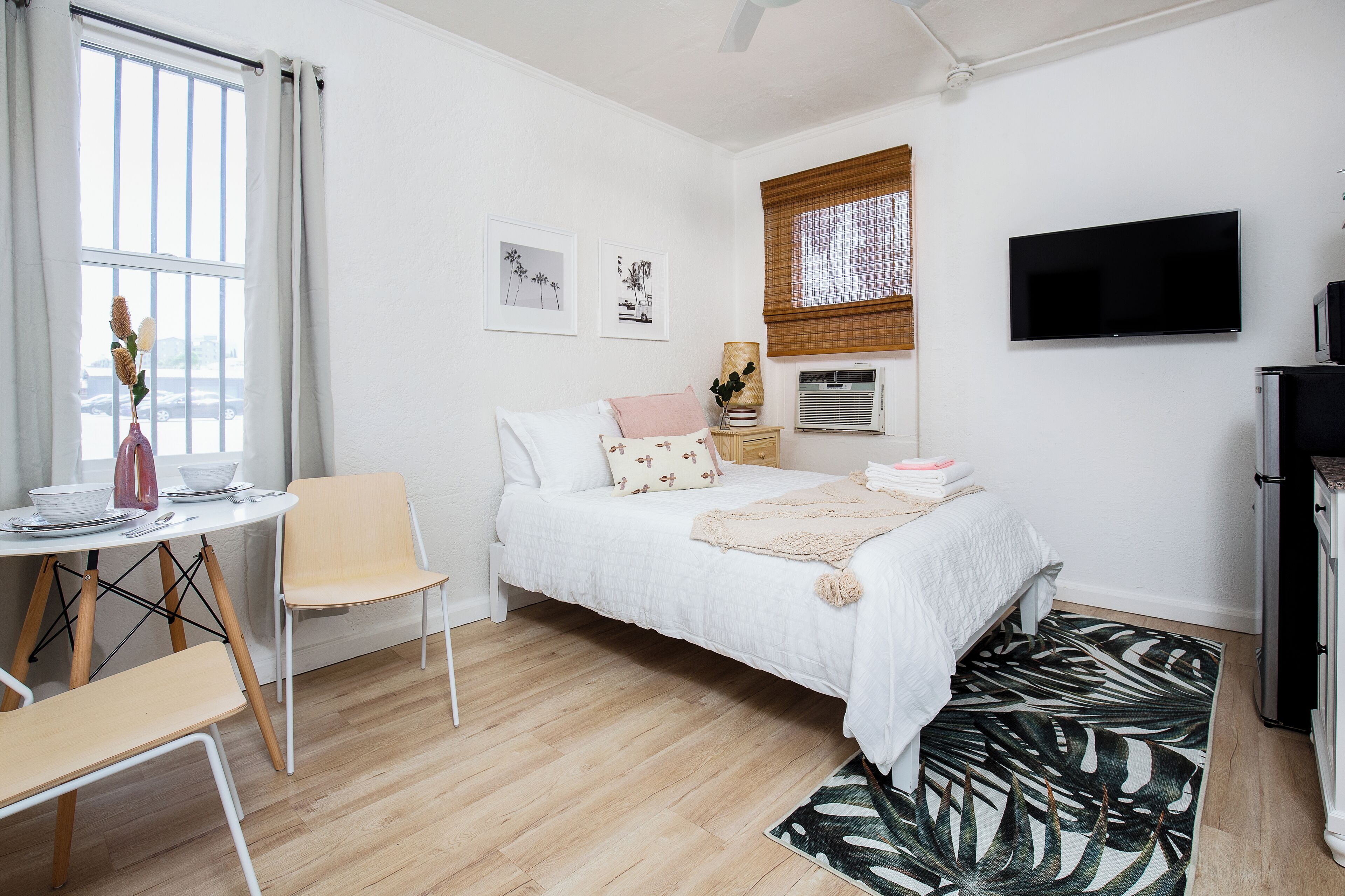 Ein Schlafzimmer mit Bett, Schreibtisch, Stuhl, Fernseher und einem Fenster mit Vorhängen.
