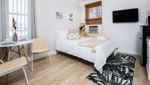 Ein Schlafzimmer mit Bett, Schreibtisch, Stuhl, Fernseher und einem Fenster mit Vorhängen.
