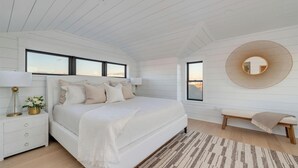 Una camera da letto con un letto grande, un comodino con una lampada, una panca e uno specchio rotondo appeso al muro.