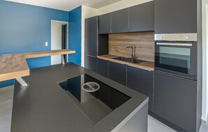 A modern kitchen with dark cabinetry, a wooden countertop, and a built-in oven. - Maison Campagne Normandie (Elbeuf-sur-Andelle)