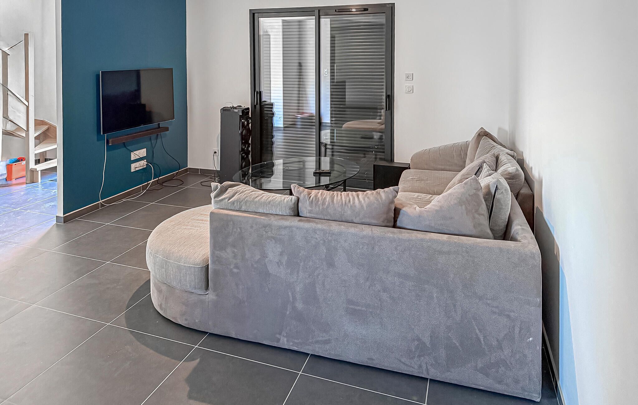 A modern living room with a grey sofa, a glass coffee table, and a flat-screen TV mounted on the wall.