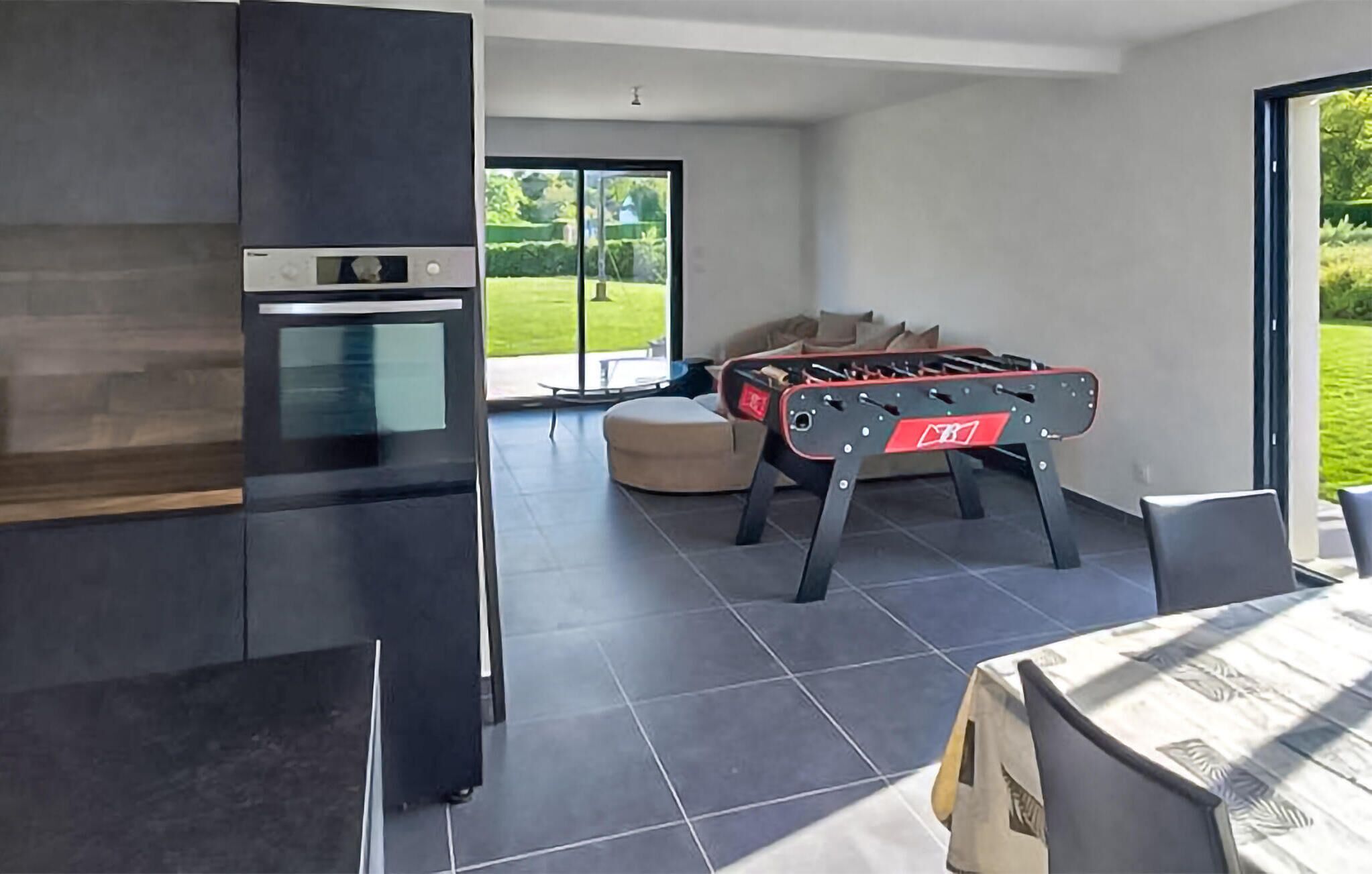 A modern kitchen with a built-in oven and a foosball table in a bright room with large windows.