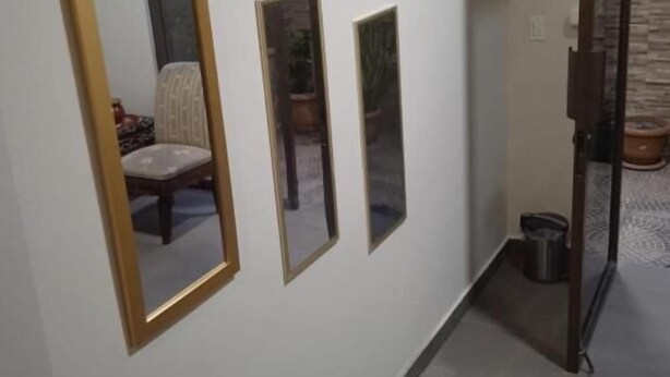 Un corridoio con un grande specchio ovale, due specchi rettangolari e una porta vetrata che dà su una stanza con parete in pietra.