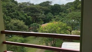 Un balcone con ringhiera rossa affacciato su un paesaggio verde e rigoglioso, con alberi e un edificio a tetto rosso.
