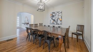 A dining room with a wooden table and chairs, a chandelier, and a large abstract painting on the wall. - The Complex on Bobbins Mill (Athens)