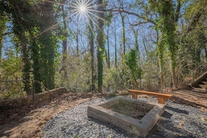 A natural outdoor area with a stone fire pit and a wooden bench. - The Complex on Bobbins Mill (Athens)