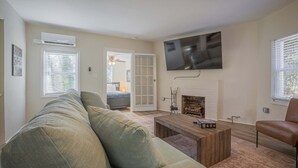A living room with a sofa, coffee table, TV, fireplace, and a door leading to another room. - The Complex on Bobbins Mill (Athens)