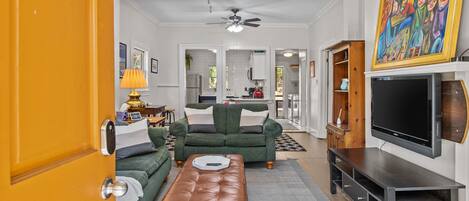 A living room with a sofa, ottoman, TV stand, and a painting.