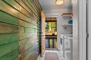 Ein schmaler Korridor mit Holzwänden und Fliesenboden, der zu einer Tür mit Blick auf einen Balkon führt.