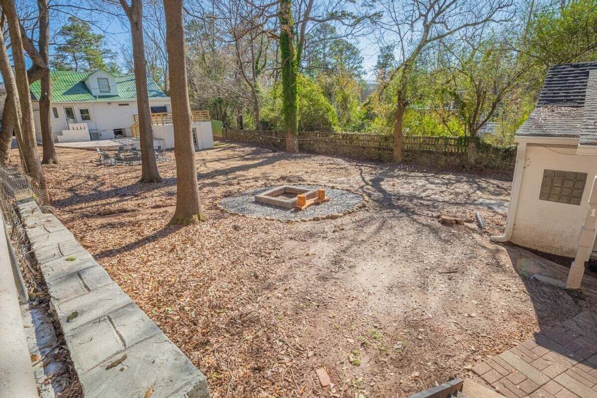A backyard with a circular fire pit, a brick wall, and a house with a green roof in the background.