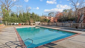 A rectangular swimming pool with a wooden deck surrounding it, a metal ladder, and a wooden fence. - Classic City Getaway at Stadium Village (Athens)