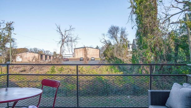A balcony with a table and chairs, a sofa, and a view of buildings and trees. - Classic City Getaway at Stadium Village (Athens)