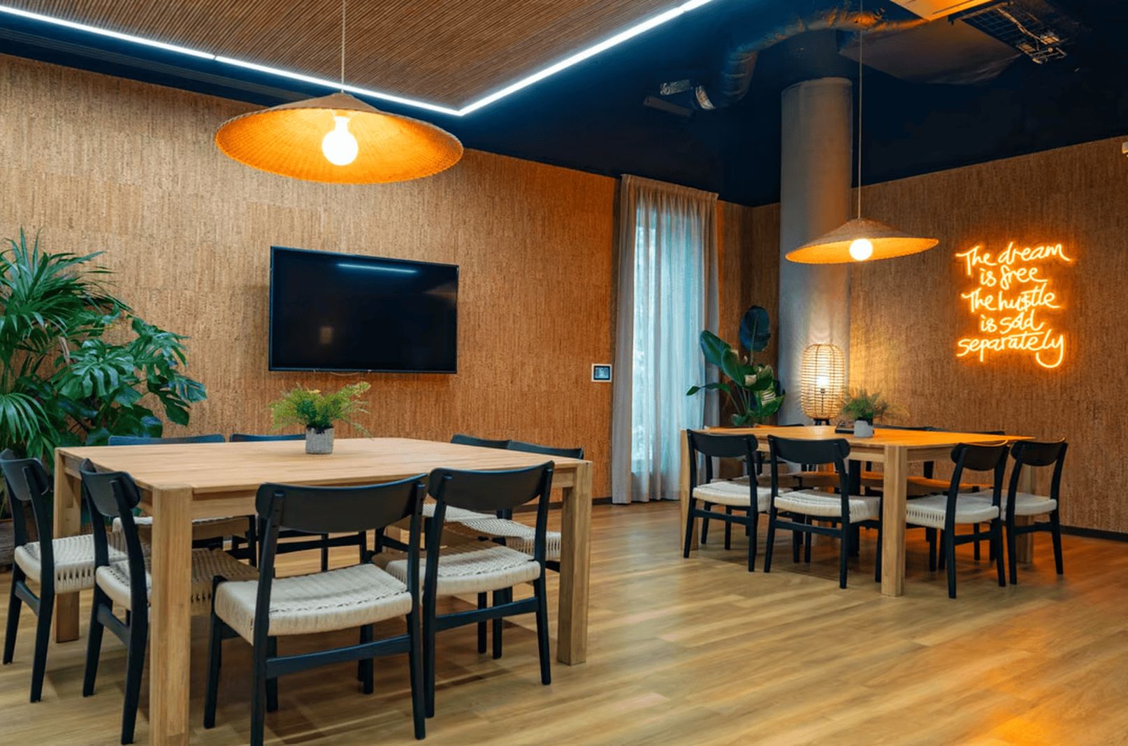 A modern conference room with wooden tables and chairs, a flat-screen TV, and a neon sign on the wall.