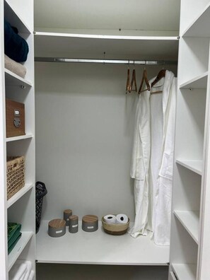 A walk-in closet with shelves, a hanging robe, and storage bins. - Air-conditioned family home (Cachoeira do Bom Jesus)
