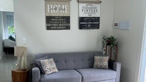 A living room with a grey sofa, two pillows, a small side table, and a potted plant. - Air-conditioned family home (Cachoeira do Bom Jesus)
