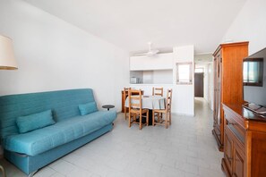 A living room with a blue sofa, a dining table with chairs, a TV stand, and a ceiling fan. - AS26823- P2 City Center - Side Sea View (LE GRAU DU ROI)