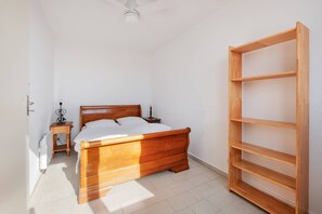 Ein Schlafzimmer mit einem hölzernen Bett, einem Nachttisch, einem an der Wand befestigten Regal und einem Deckenventilator.