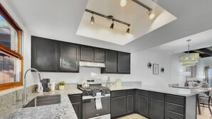 A modern kitchen with dark cabinets, a granite countertop, a stainless steel stove, and a skylight. - 3BR patio home w community pool, heated spa (Tucson)