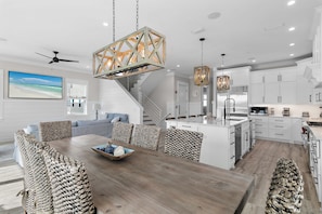 A modern kitchen with white cabinetry, a wooden dining table, and a large island. - Gulf-View Luxury with Private Pool & Beach Access (Panama City Beach)