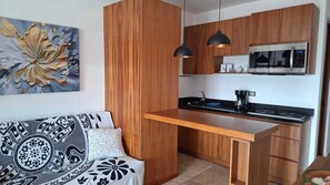 Eine kompakte Küche mit Holzausstattung, einer eingebauten Mikrowelle und einer schwarzen Arbeitsplatte.